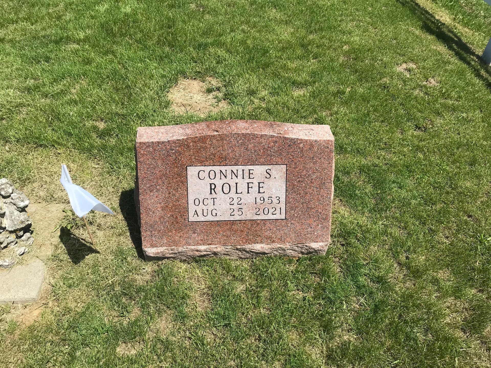 A gravestone for Connie Rolfe is sitting in the grass in a cemetery.