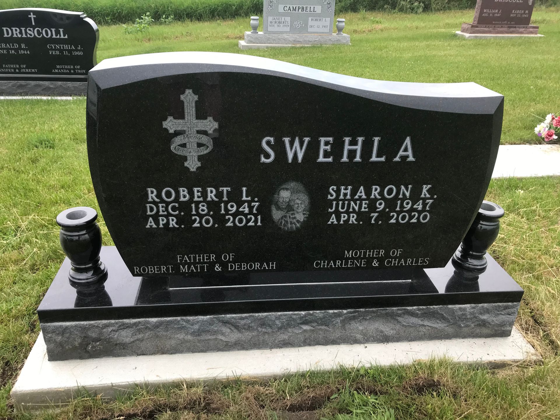 A black gravestone with a cross on it is in a cemetery.