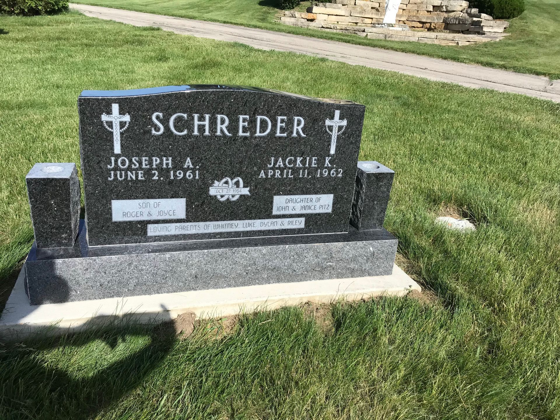 A black gravestone with a cross on it is in a cemetery.