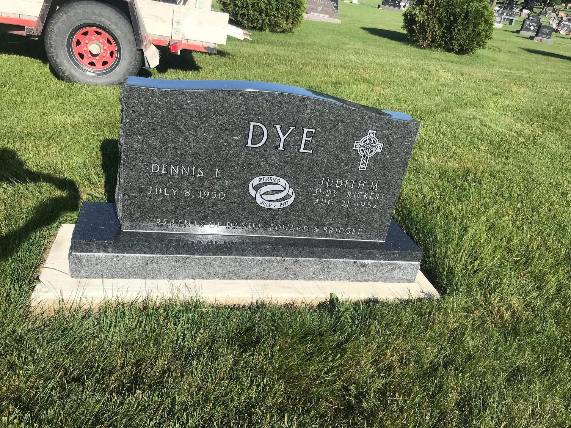 A gravestone in a cemetery with a truck in the background.