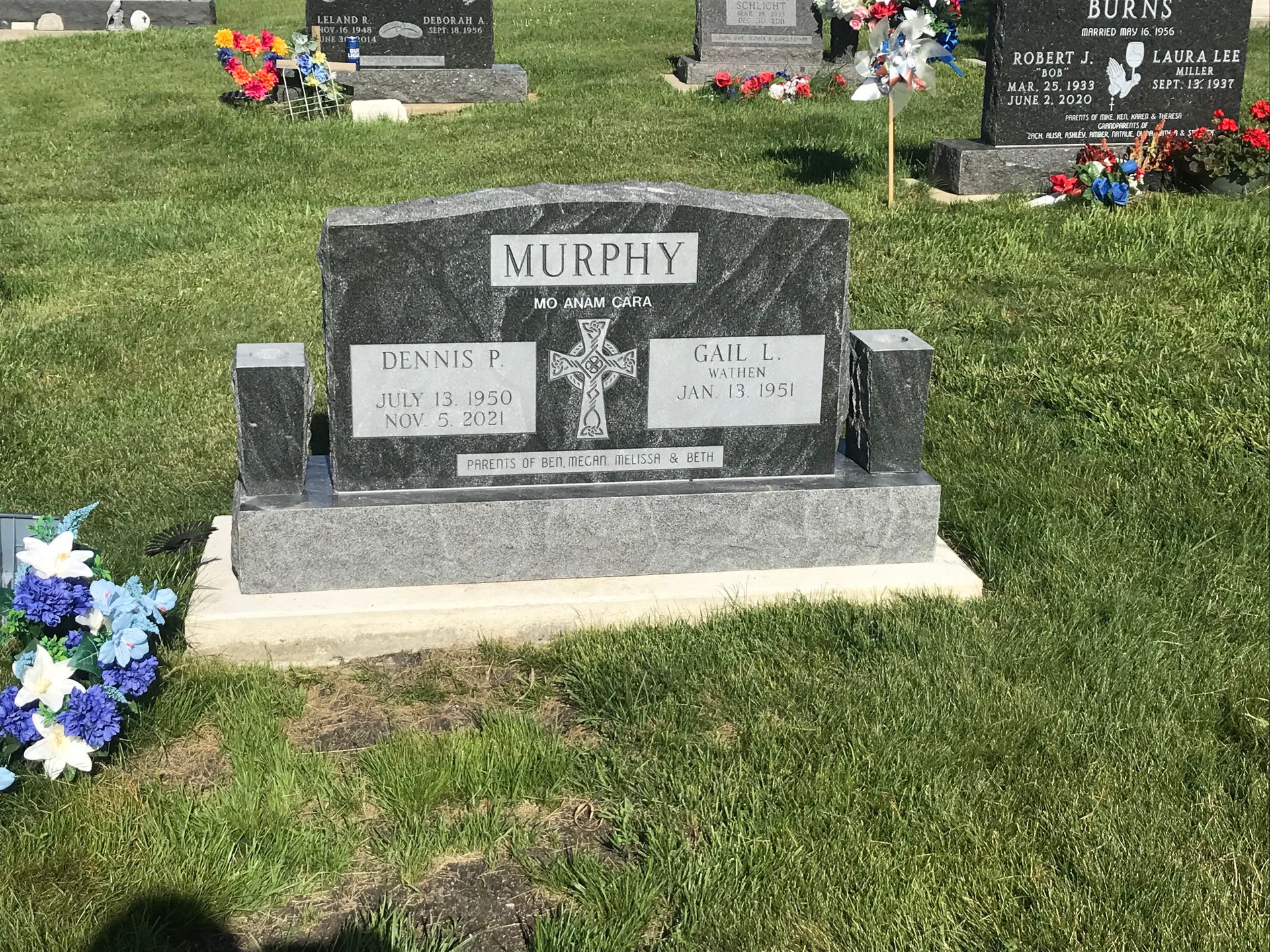 A grave in a cemetery with flowers and a cross on it.