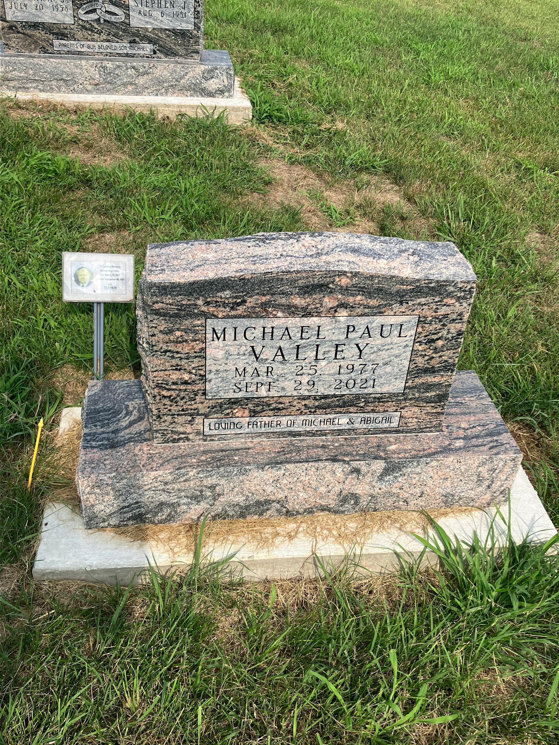 A gravestone in a cemetery with a sign on it.