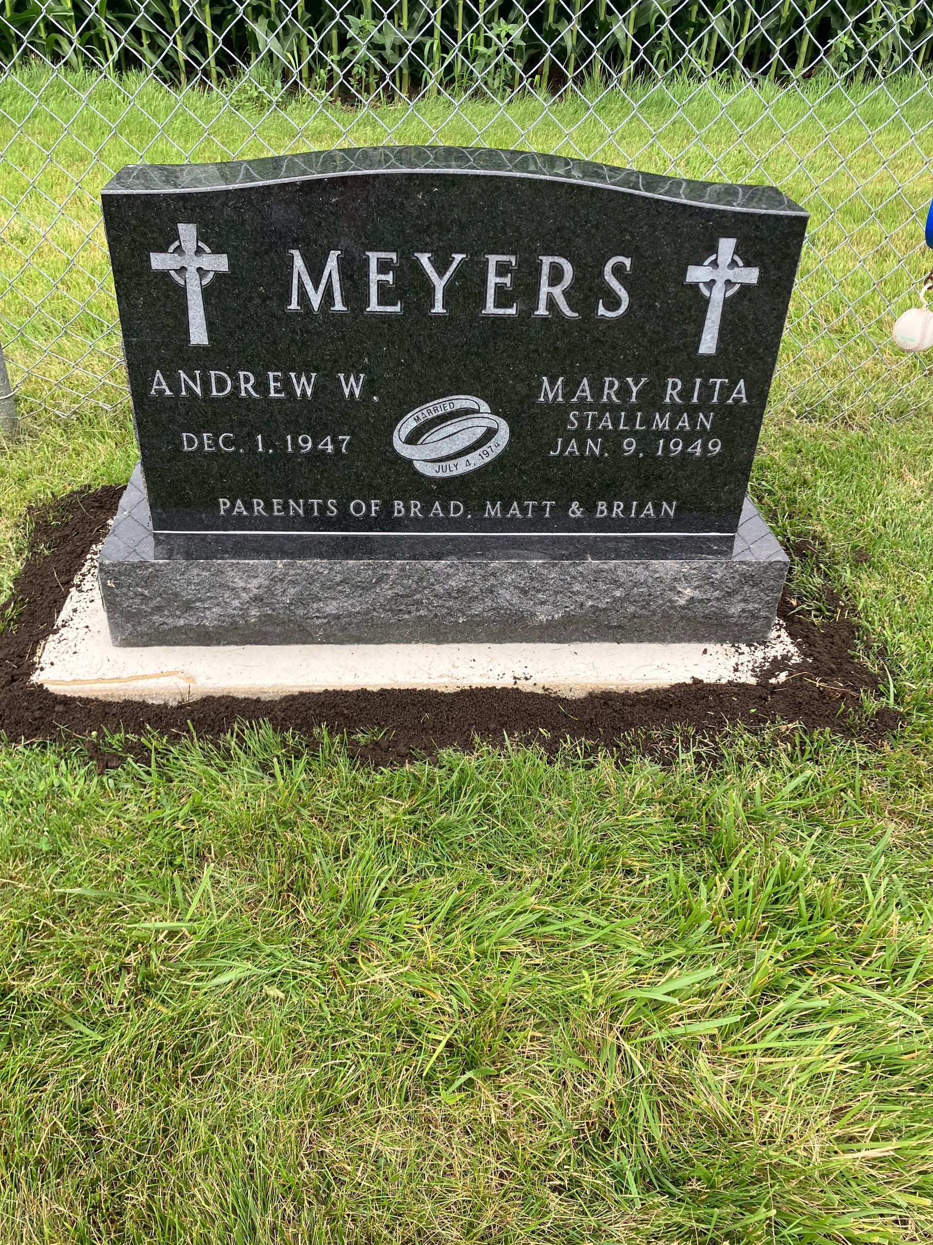 A black gravestone in a cemetery with a cross on it.