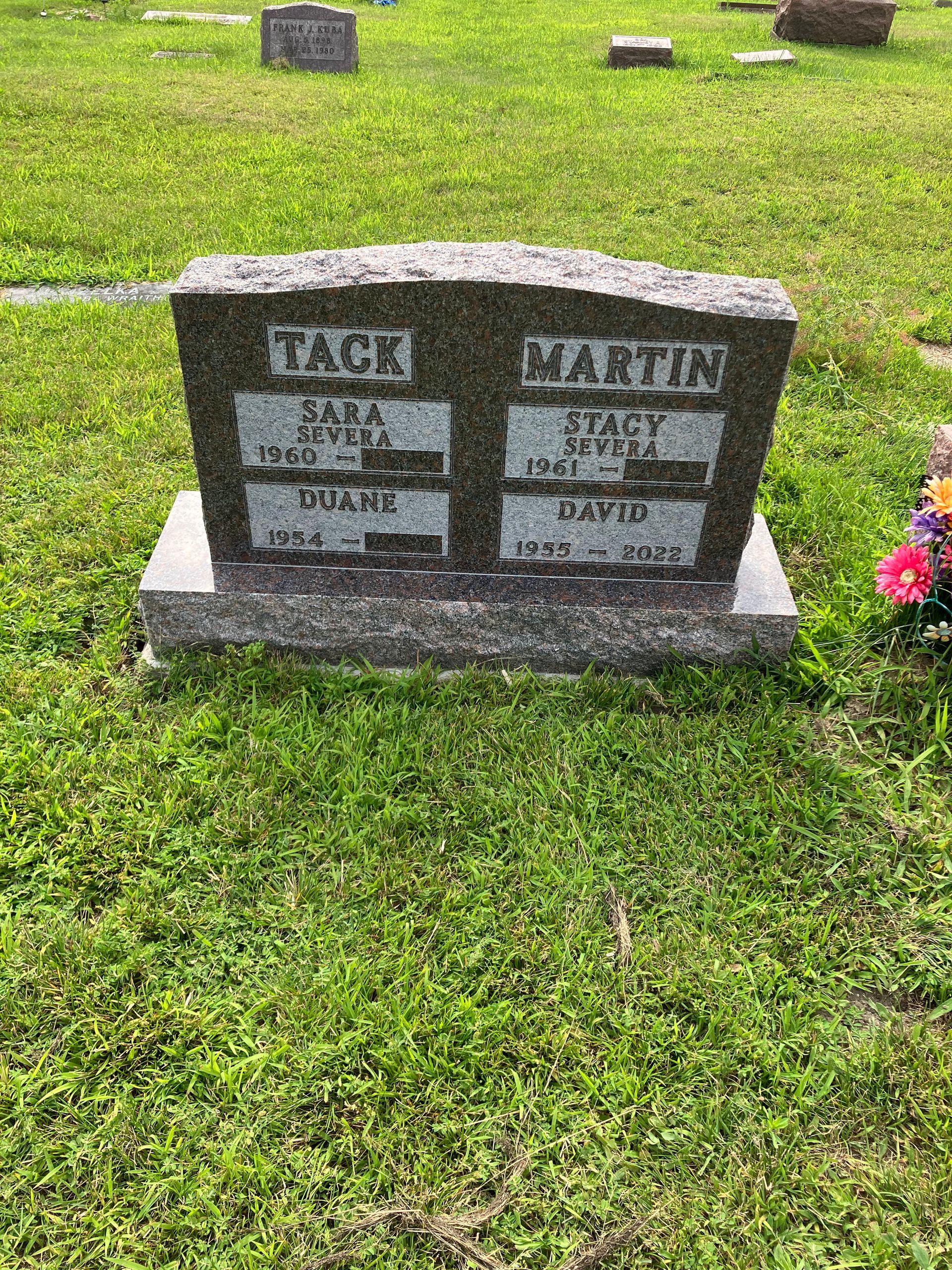 A gravestone in a cemetery with flowers in the grass.