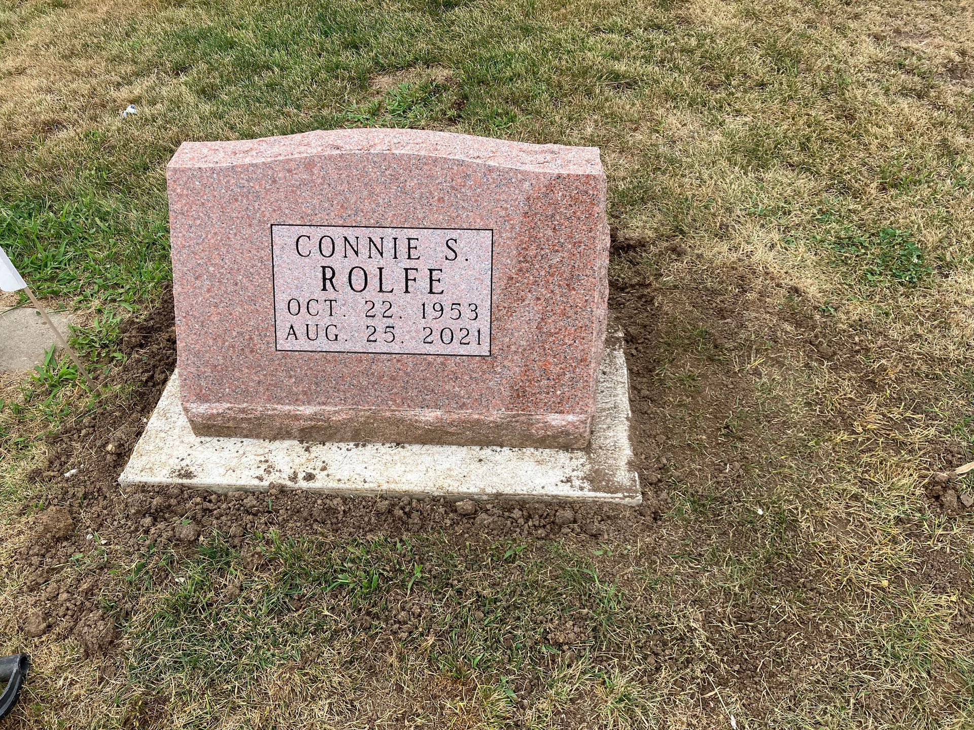 A gravestone for Connie S. Rolfe is sitting in the grass in a cemetery.
