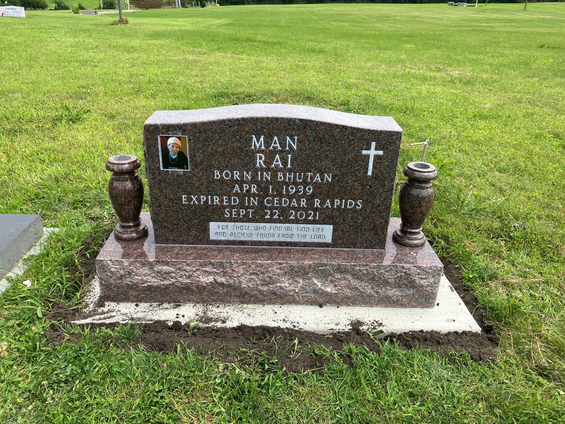 A gravestone in a cemetery with two vases and a cross on it.