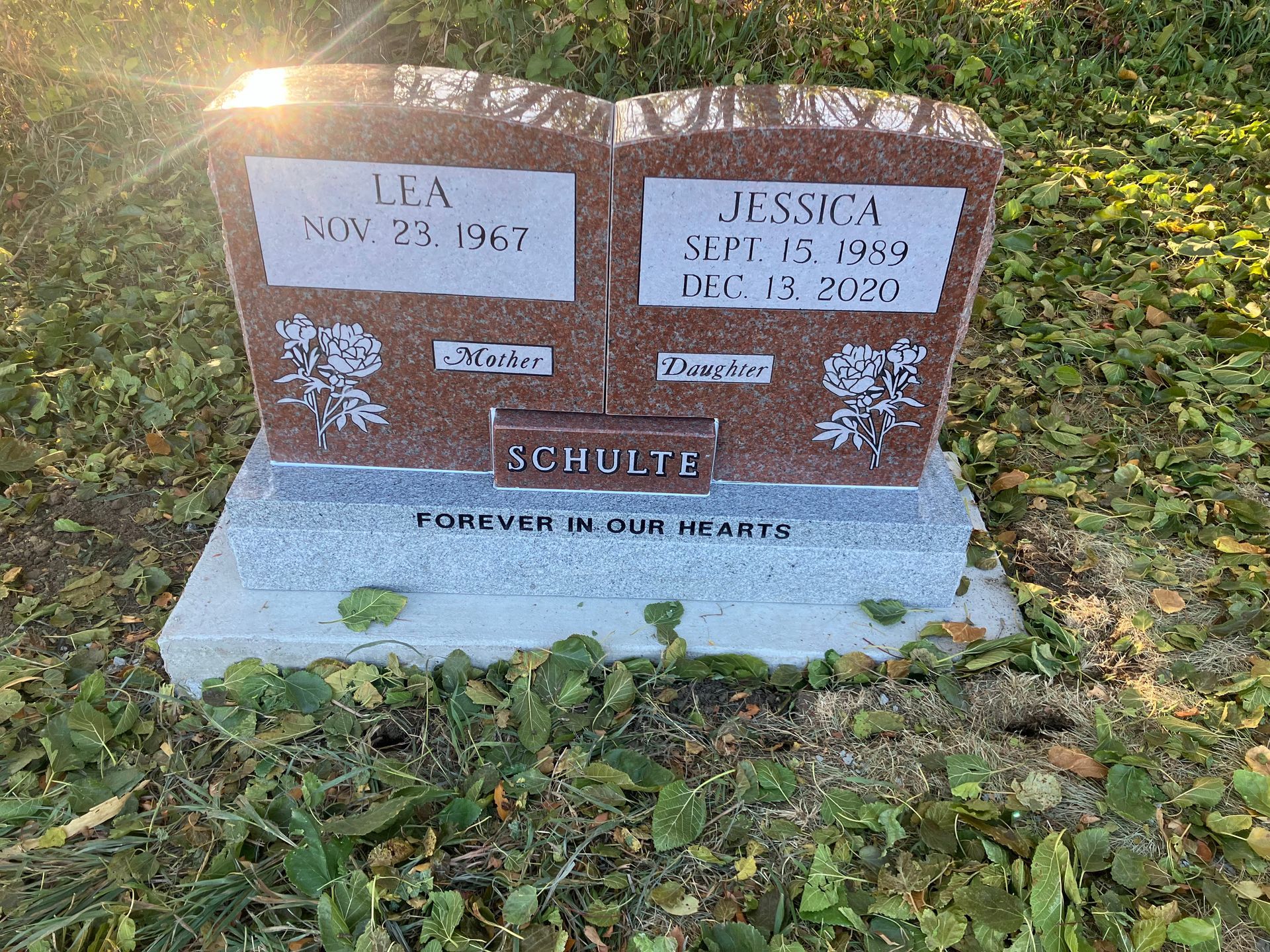 A gravestone for two people is sitting in the grass in a cemetery.