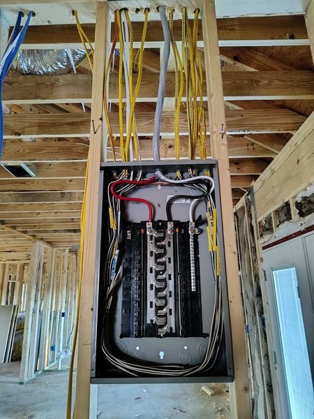 Electrical panel installed in a wooden framed wall with multiple yellow and gray wires. 