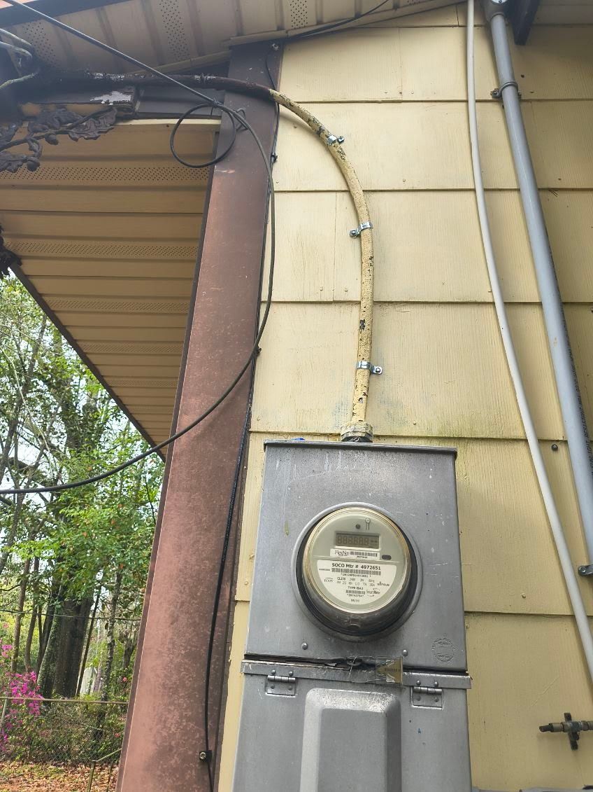An outdoor electrical meter and service cable mounted on the yellow siding of a house.