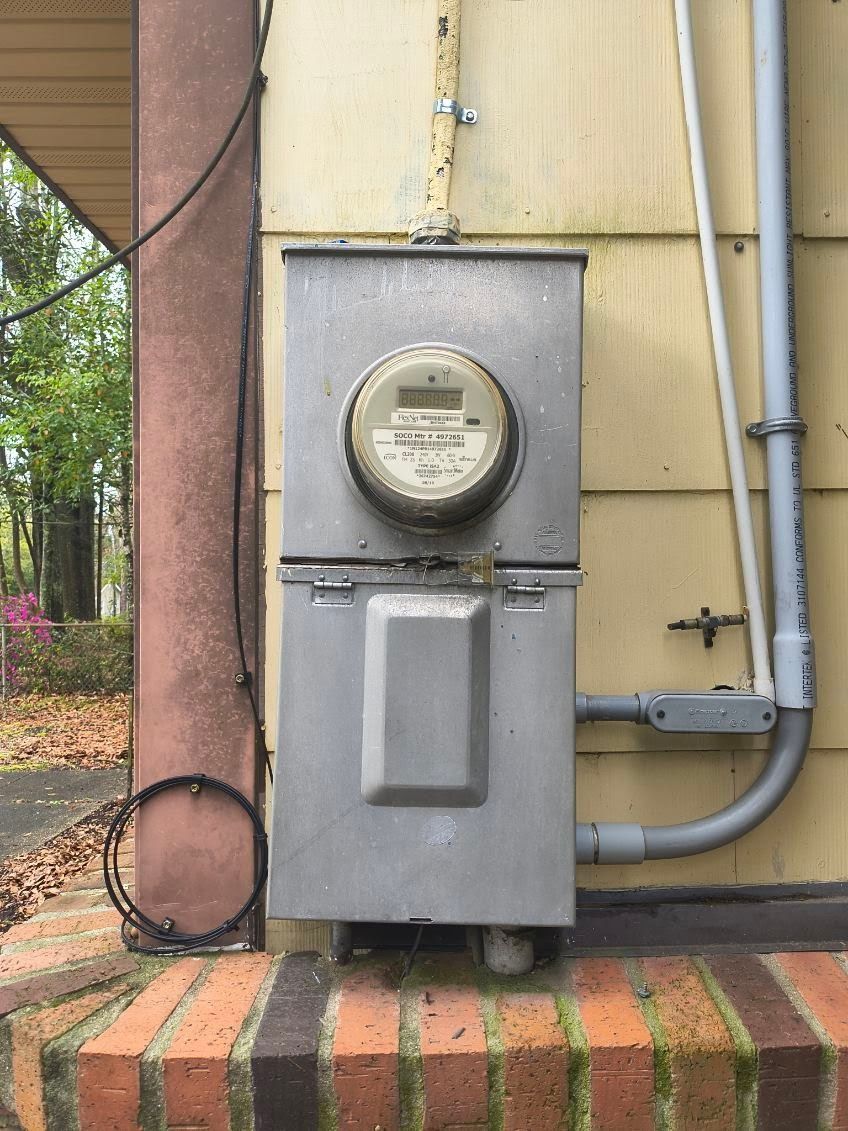 An electric meter mounted in a grey metal box on the side of a building above a brick ledge.