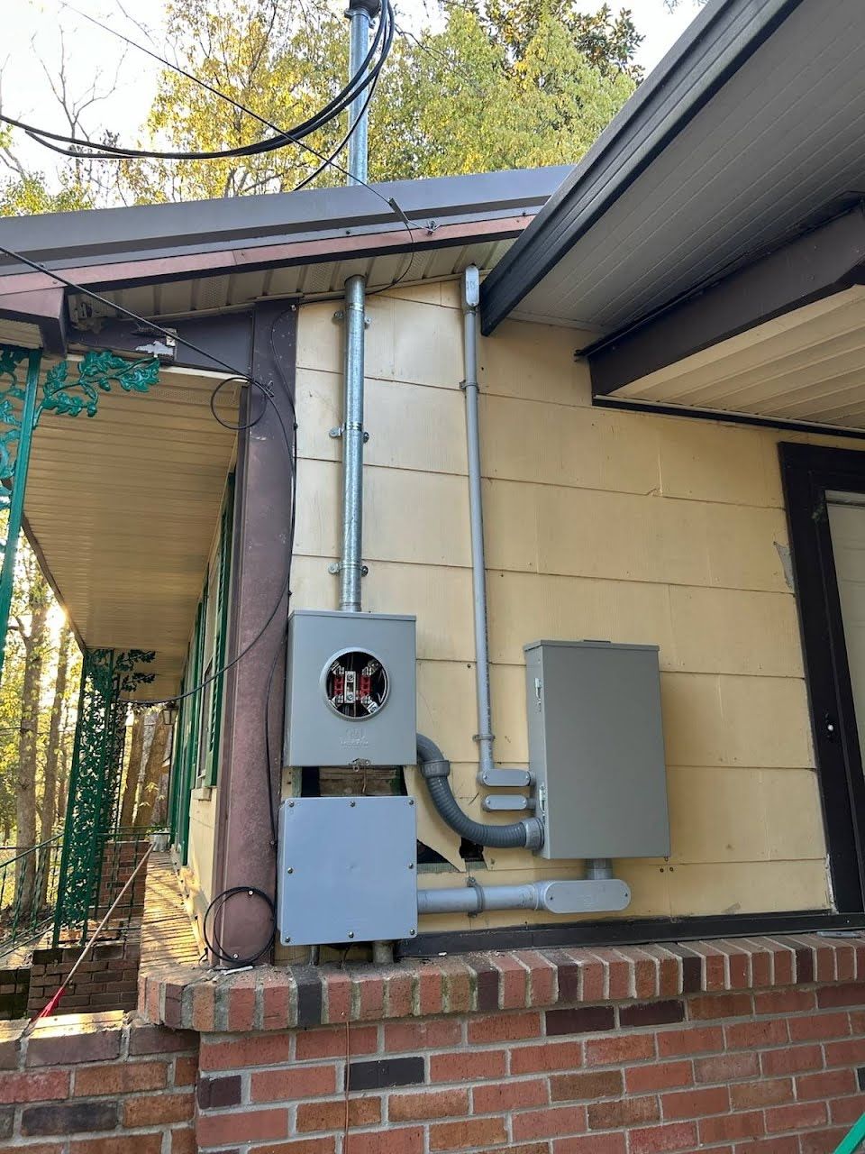 An outdoor electrical service entrance on a tan house wall featuring a meter base, junction box, and breaker panel.