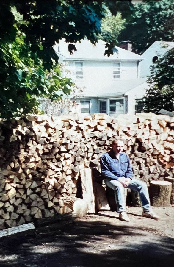 a man sits in front of a pile of firewood