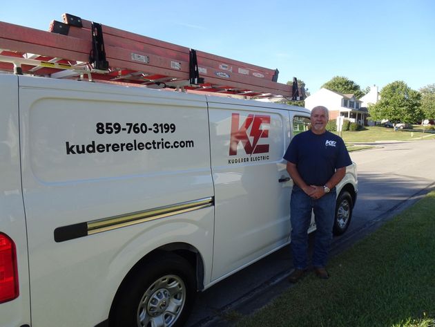White Kudere Electric van parked roadside with a man standing beside it on a sunny day