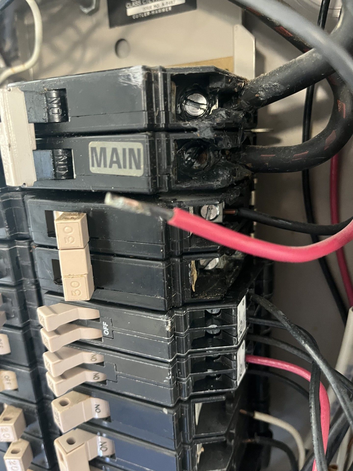 Close-up of stacked electrical circuit breakers with a cracked main breaker and red and black wires.