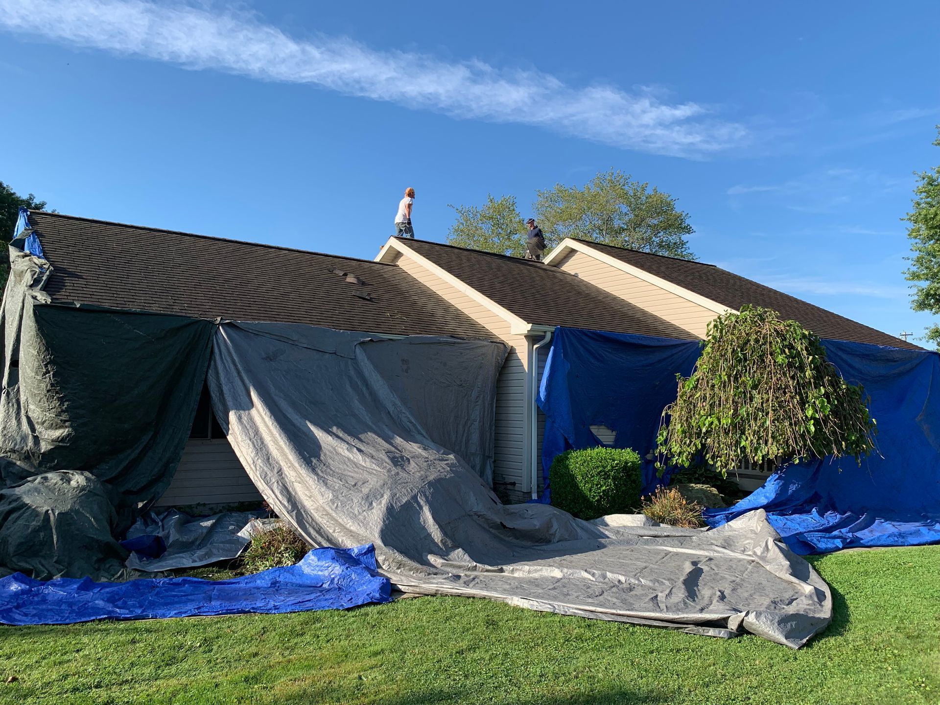A man is standing on the roof of a house covered in tarps.