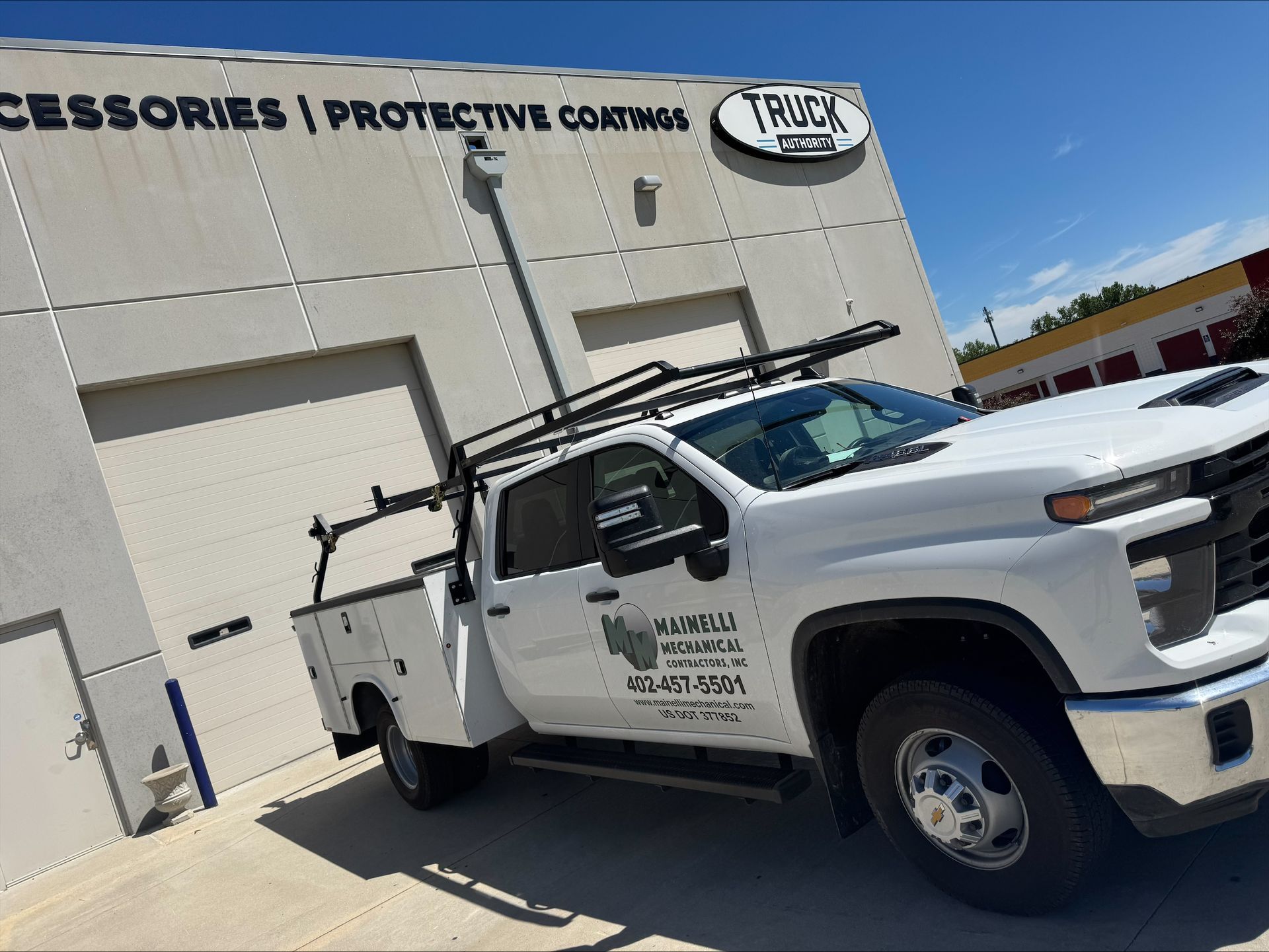 White utility truck parked outside a shop with a clear blue sky overhead.