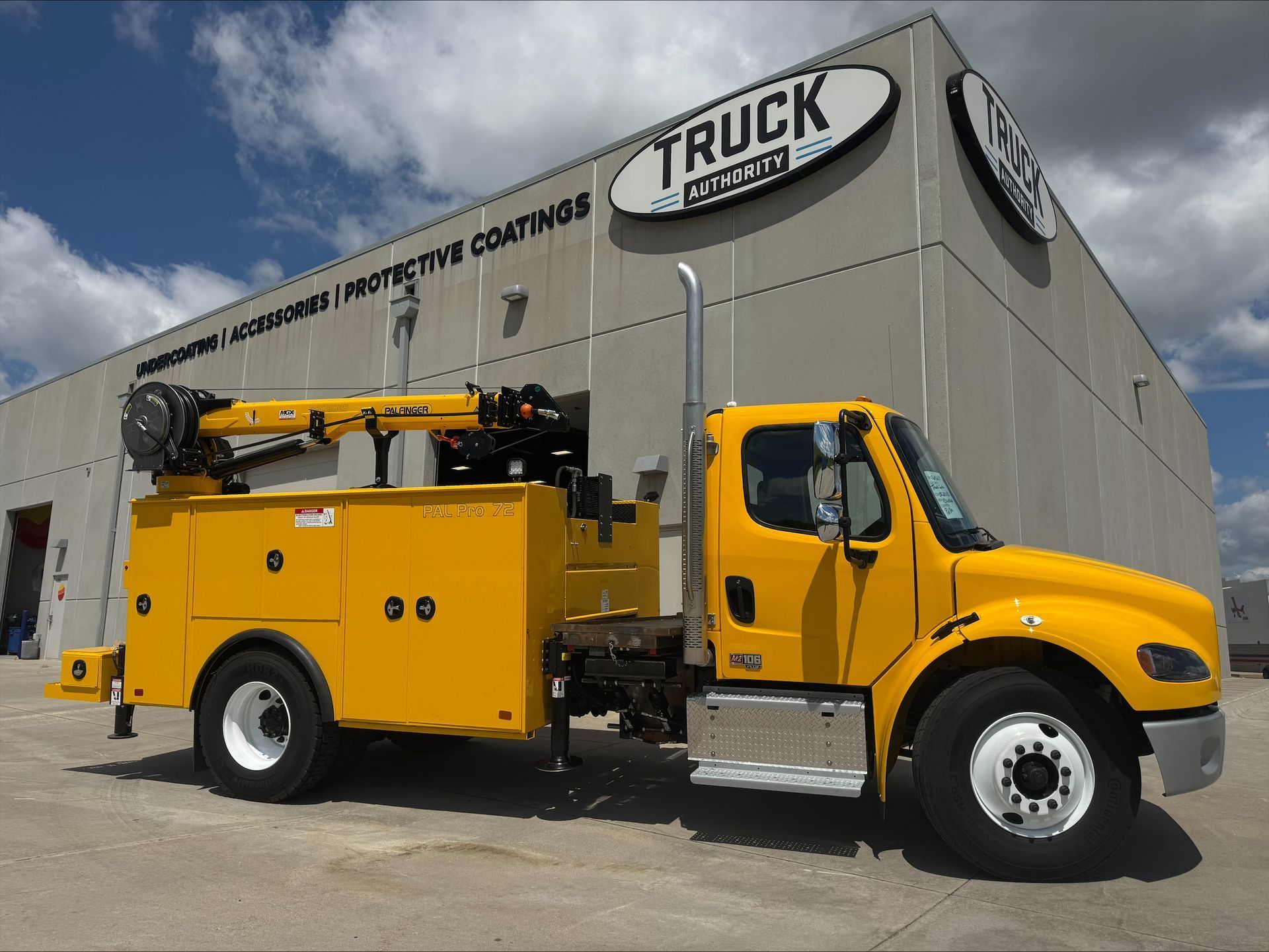 Yellow utility truck parked beside a gray building.