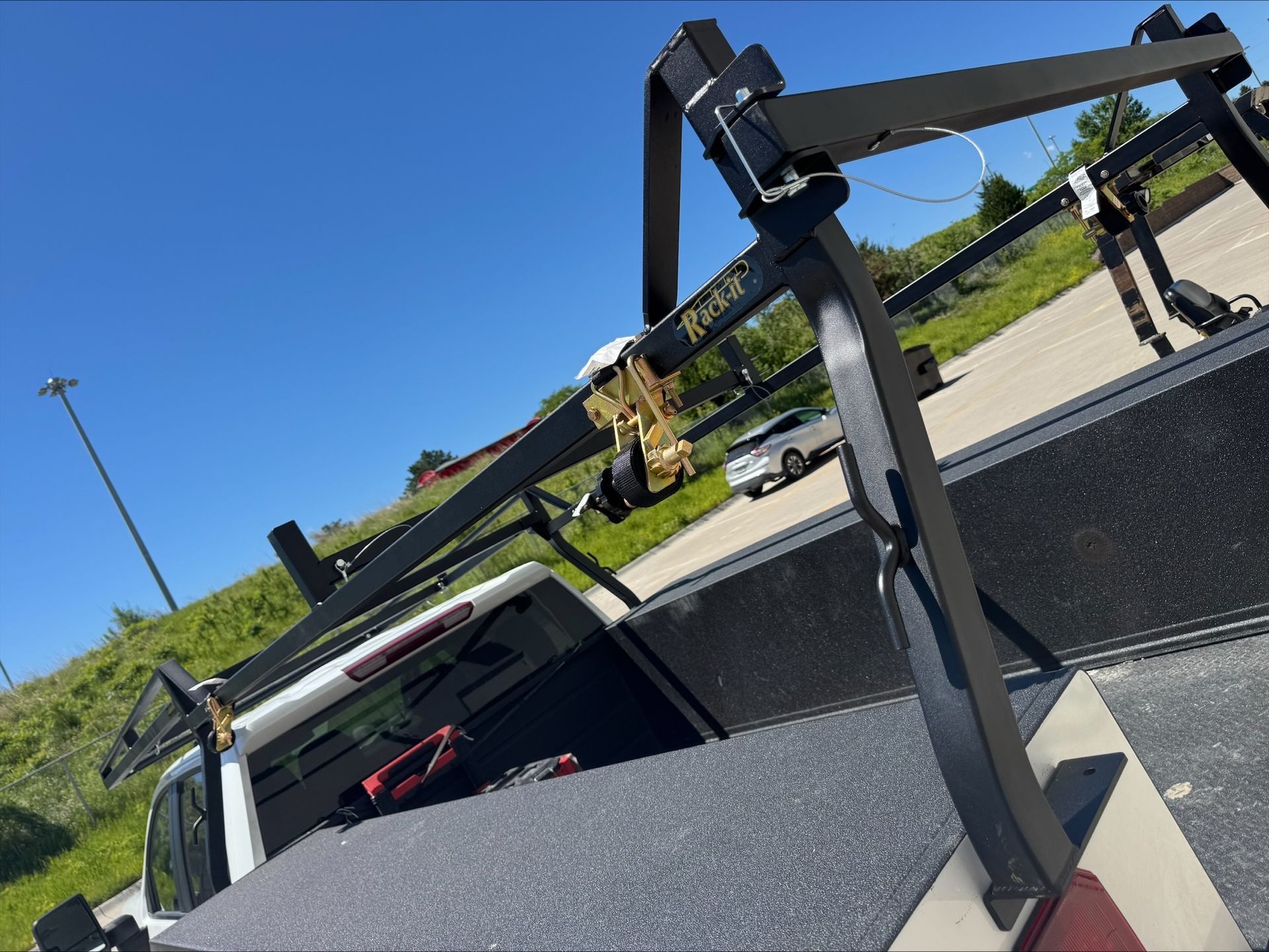 A black pickup truck with a metal bed rack parked by a sunny roadside.
