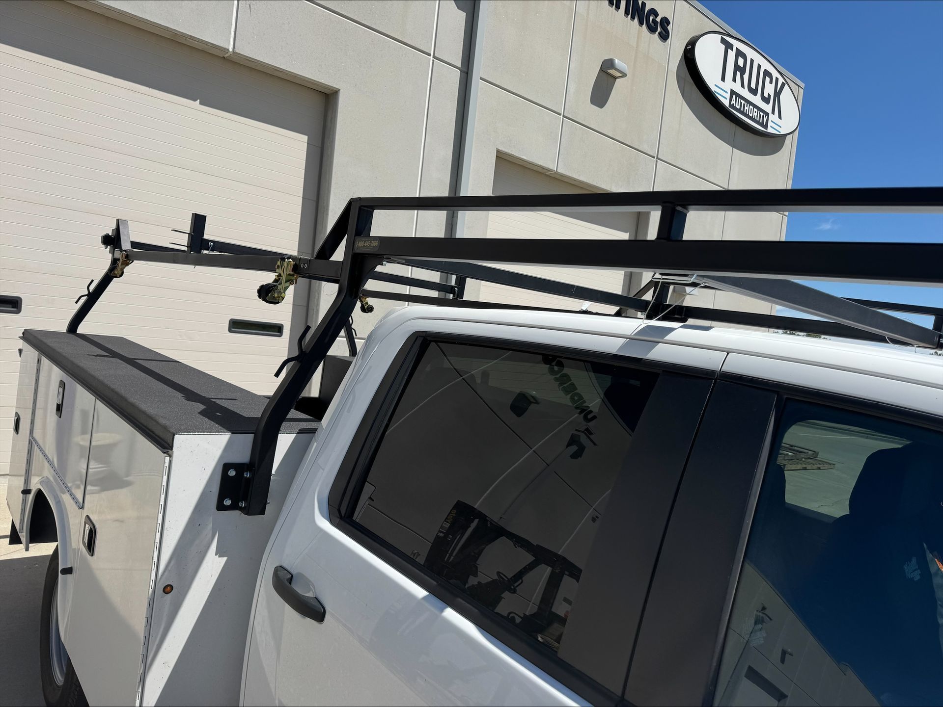 White truck with roof rack parked beside a building in sunlight.