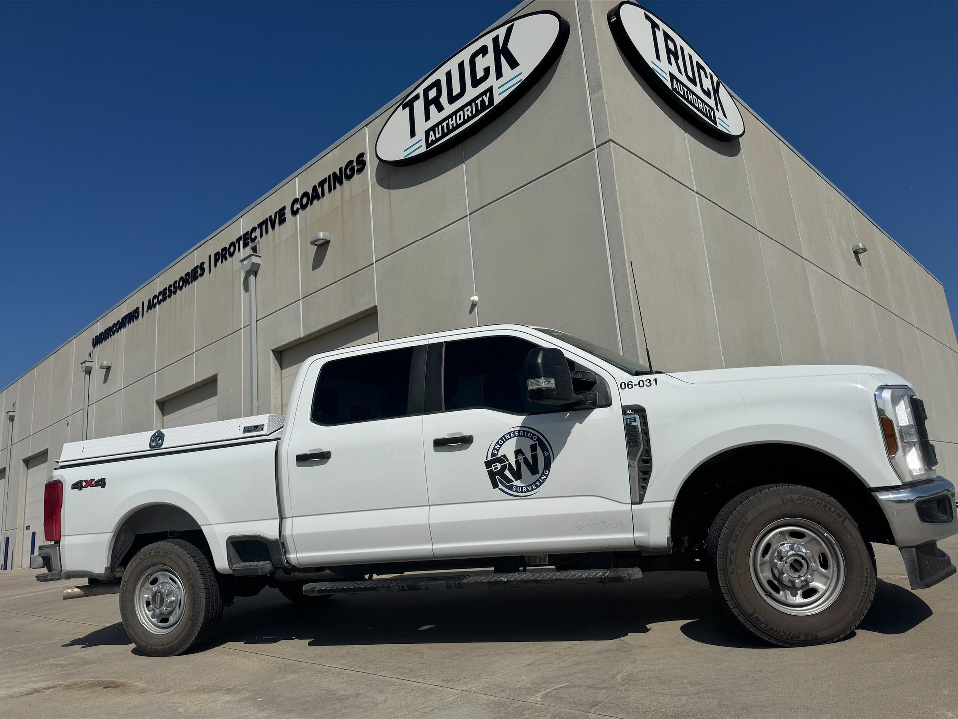 White service truck parked outside a truck repair shop on a sunny day.