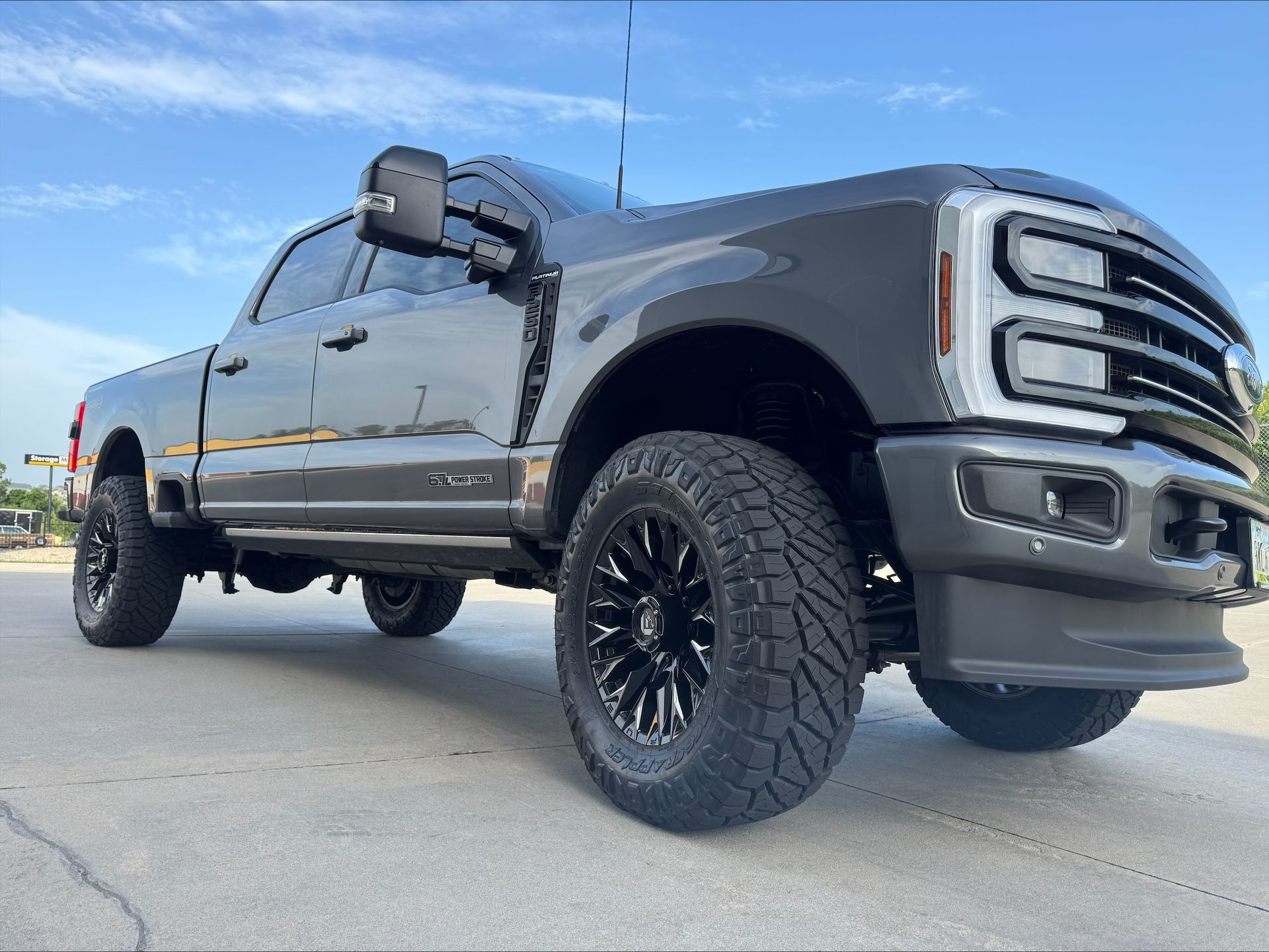Black lifted pickup truck with off-road tires parked on pavement under a blue sky.