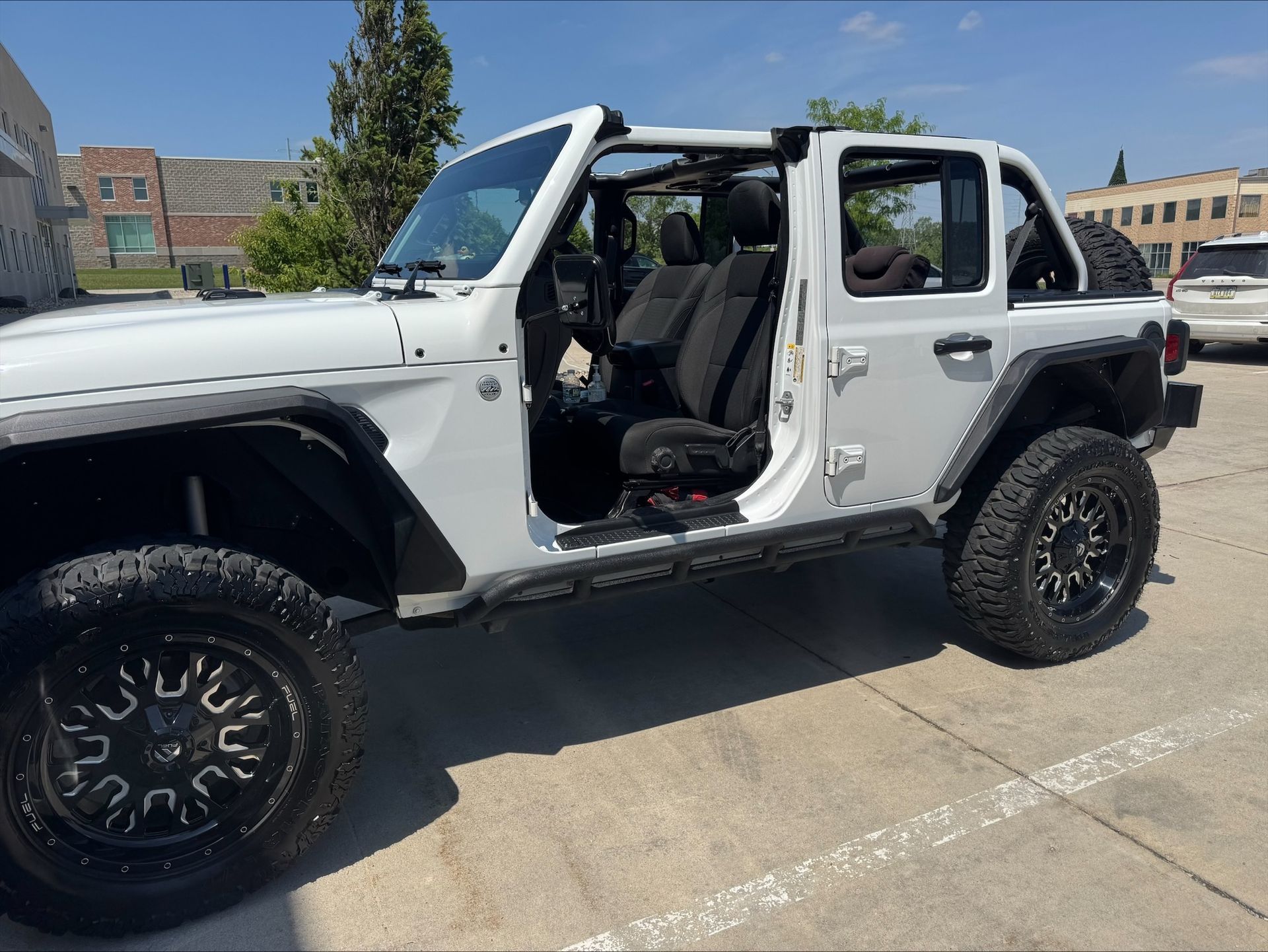 White Jeep Wrangler with no doors parked in a lot on a sunny day.