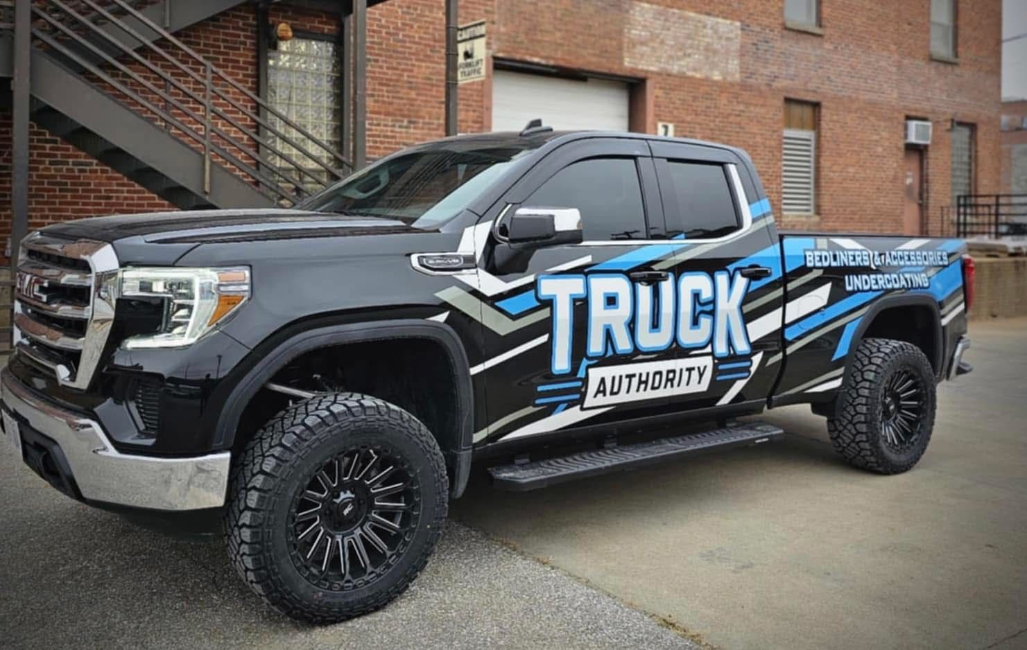 Black pickup truck with TRUCK authority graphics parked beside a brick building.
