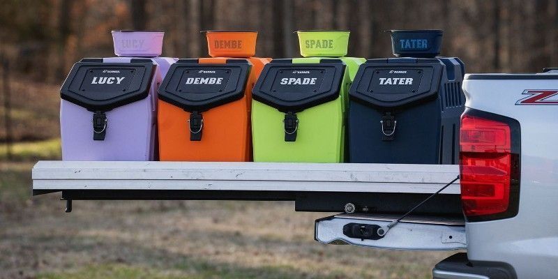 Four color-coded insulated delivery bags in a pickup truck bed with menu labels on top.