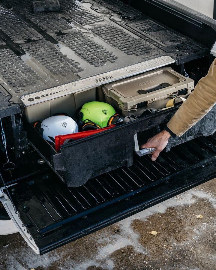 Helmets and gear stored in a truck bed compartment, with a person pulling out a tray