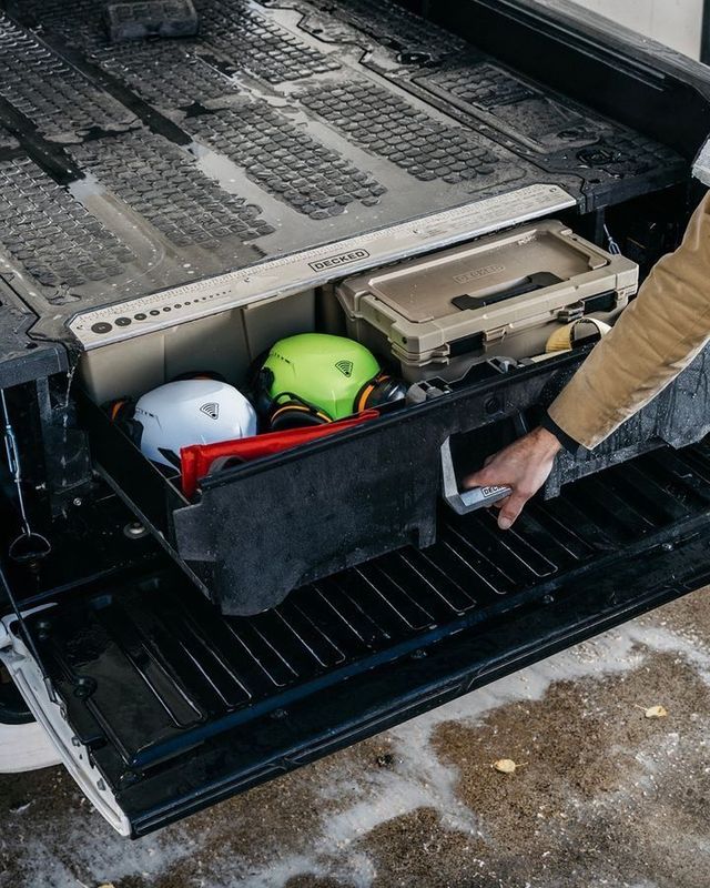 Helmets and gear stored in a truck bed compartment, with a person pulling out a tray
