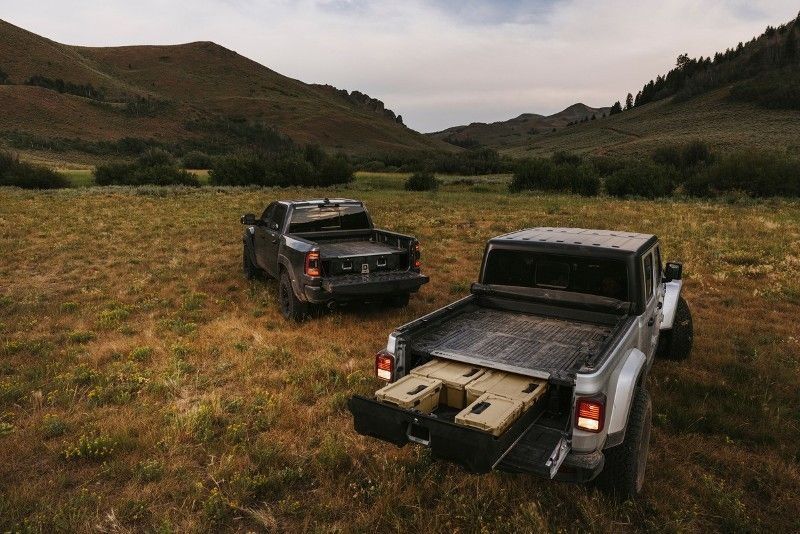 Two pickup trucks parked in a grassy mountain valley, one with an open tailgate and cargo bed