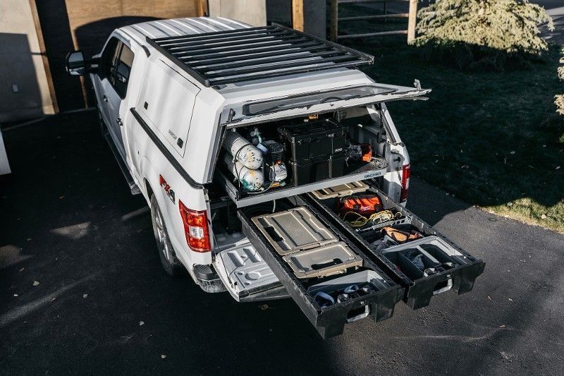 White utility van with rear cargo trays and open equipment storage in a driveway