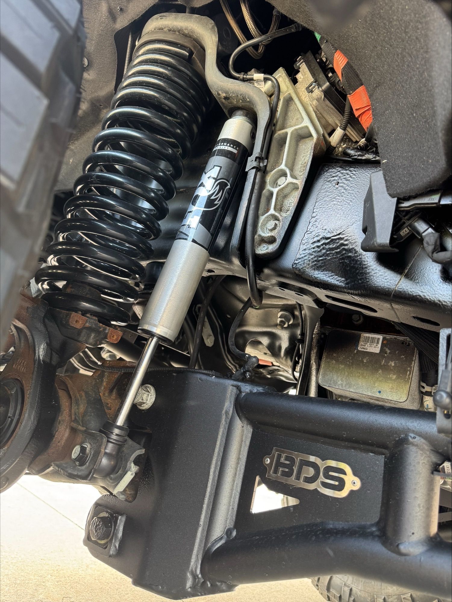 Close-up of a vehicle suspension with coil spring, shock absorber, and control arm undercarriage components.