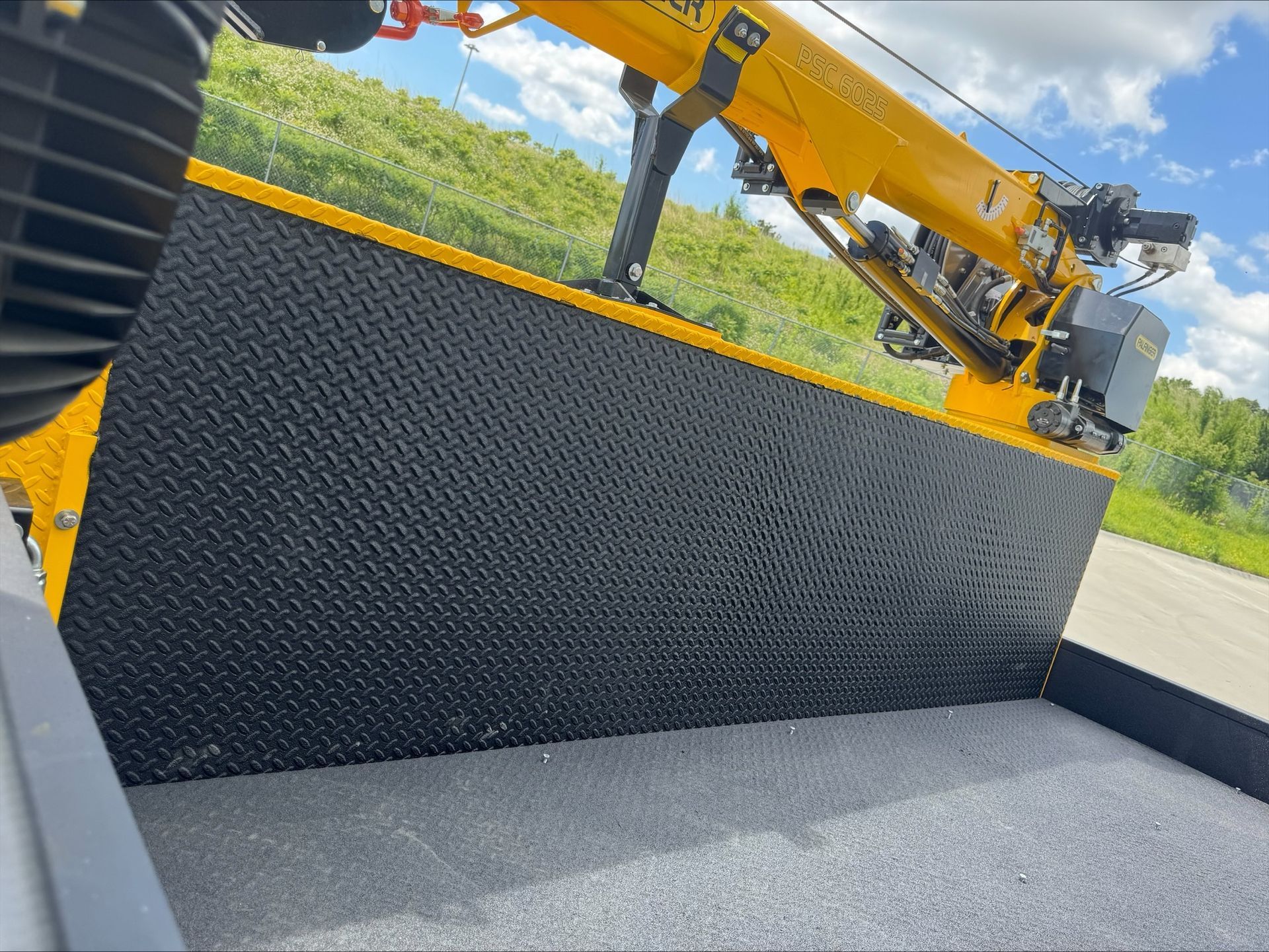 Yellow crane loading a black textured container beside an open gray platform outdoors.