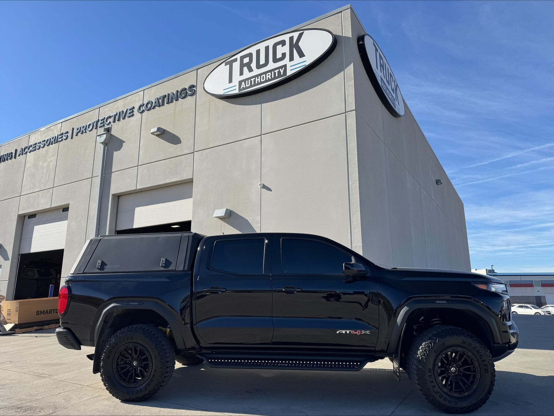 Black truck parked beside a gray commercial building under a blue sky.