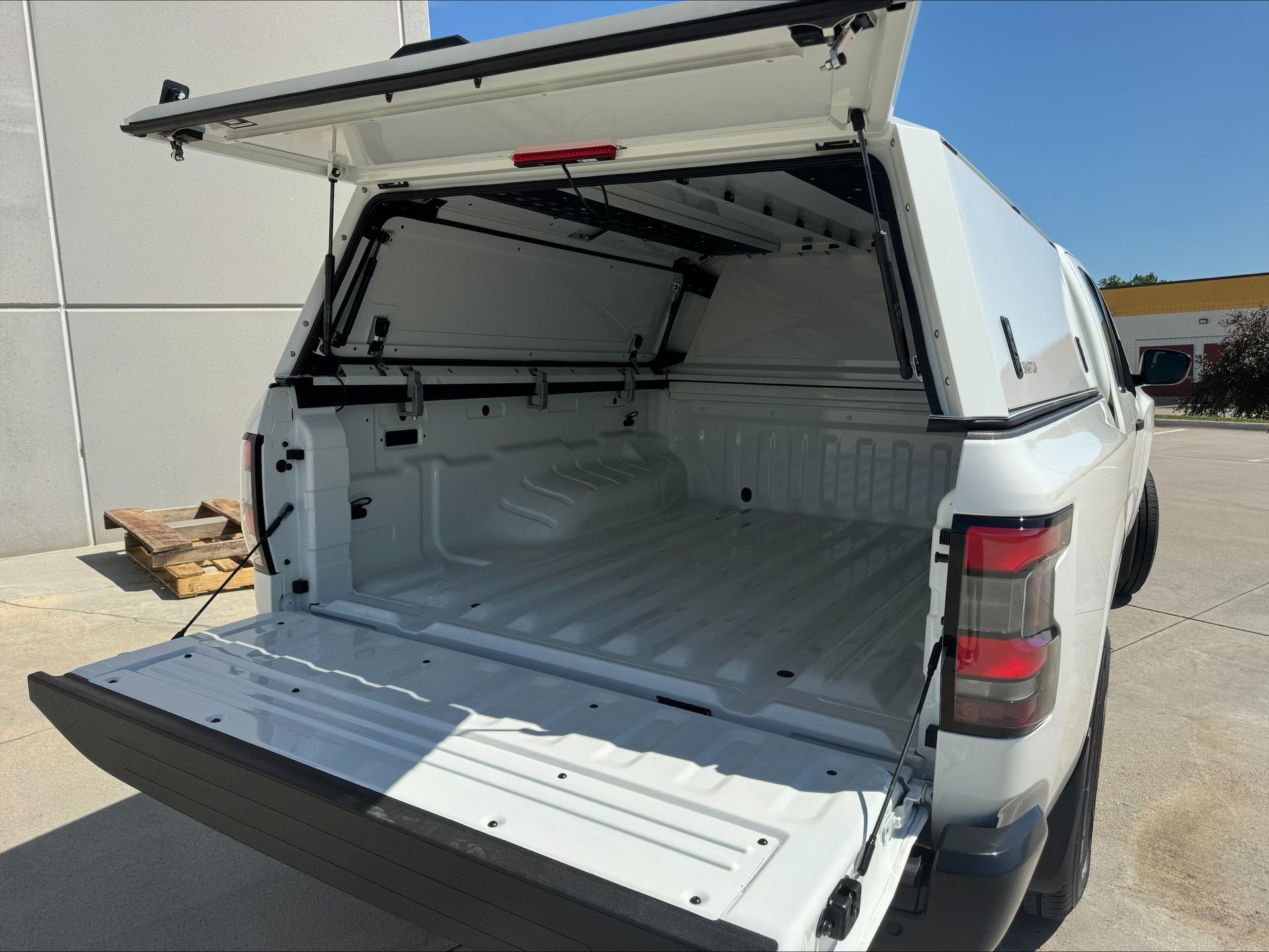 Open white utility truck bed with canopy doors lifted and tailgate down in a parking lot.