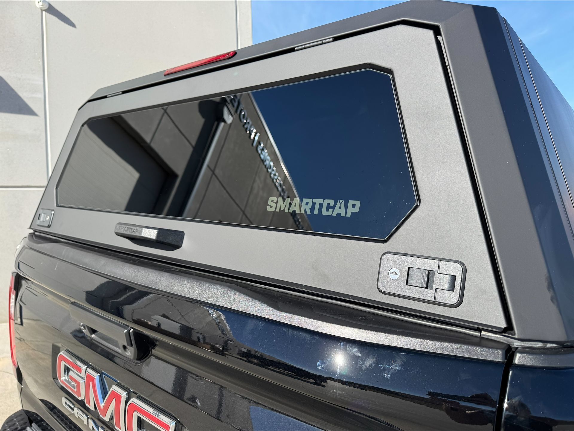 Black GMC truck with a silver SmartCap camper shell and tinted side window.