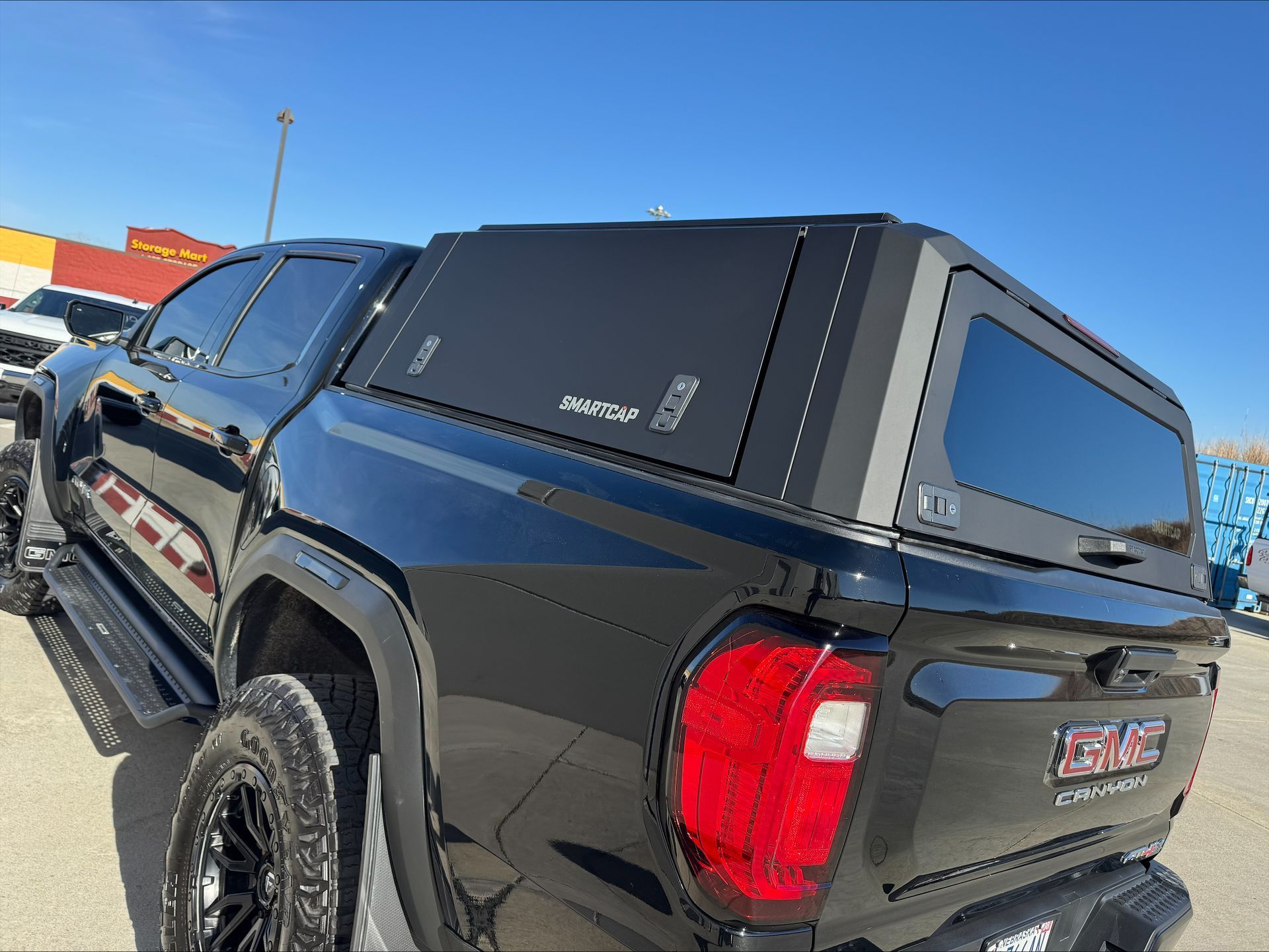 Black pickup truck with a camper shell parked outdoors under a clear blue sky.
