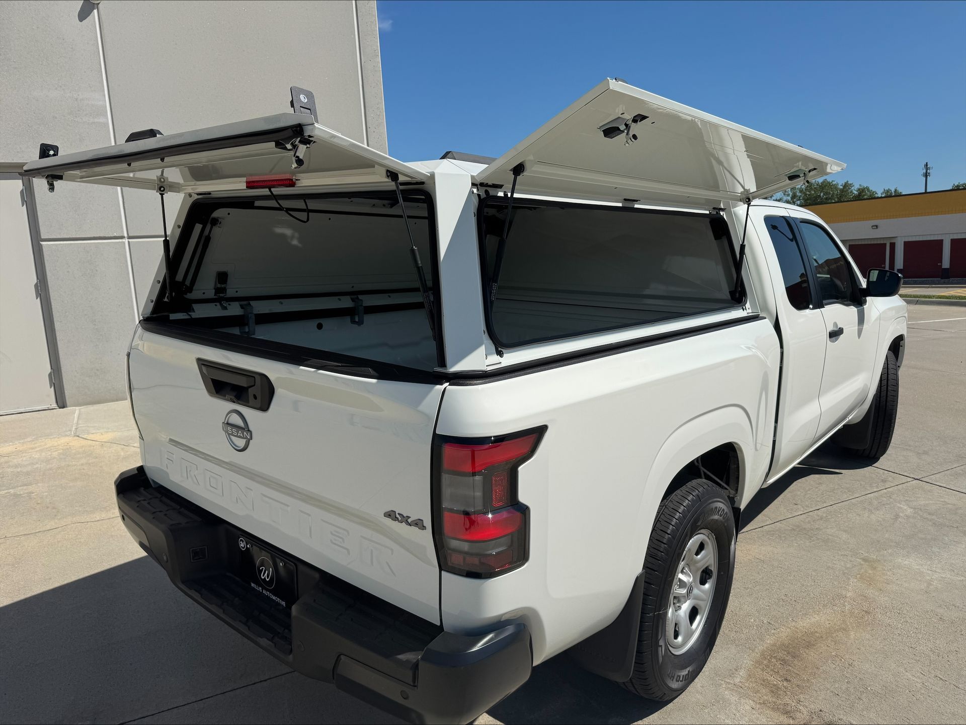 White pickup truck with open canopy panels in a parking lot, rear three-quarter view.