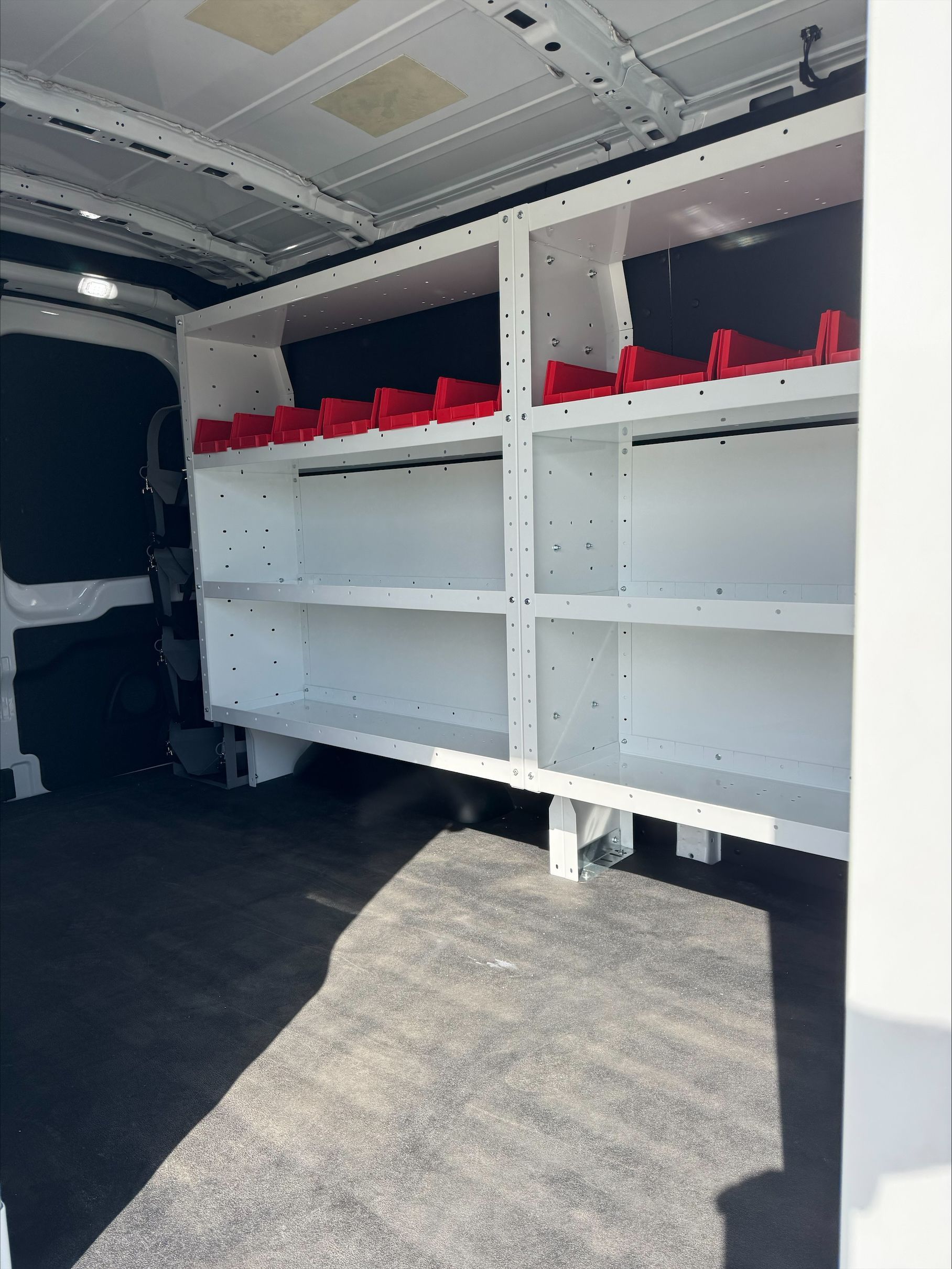 Empty white shelving inside a cargo van with red bins on the top shelves.