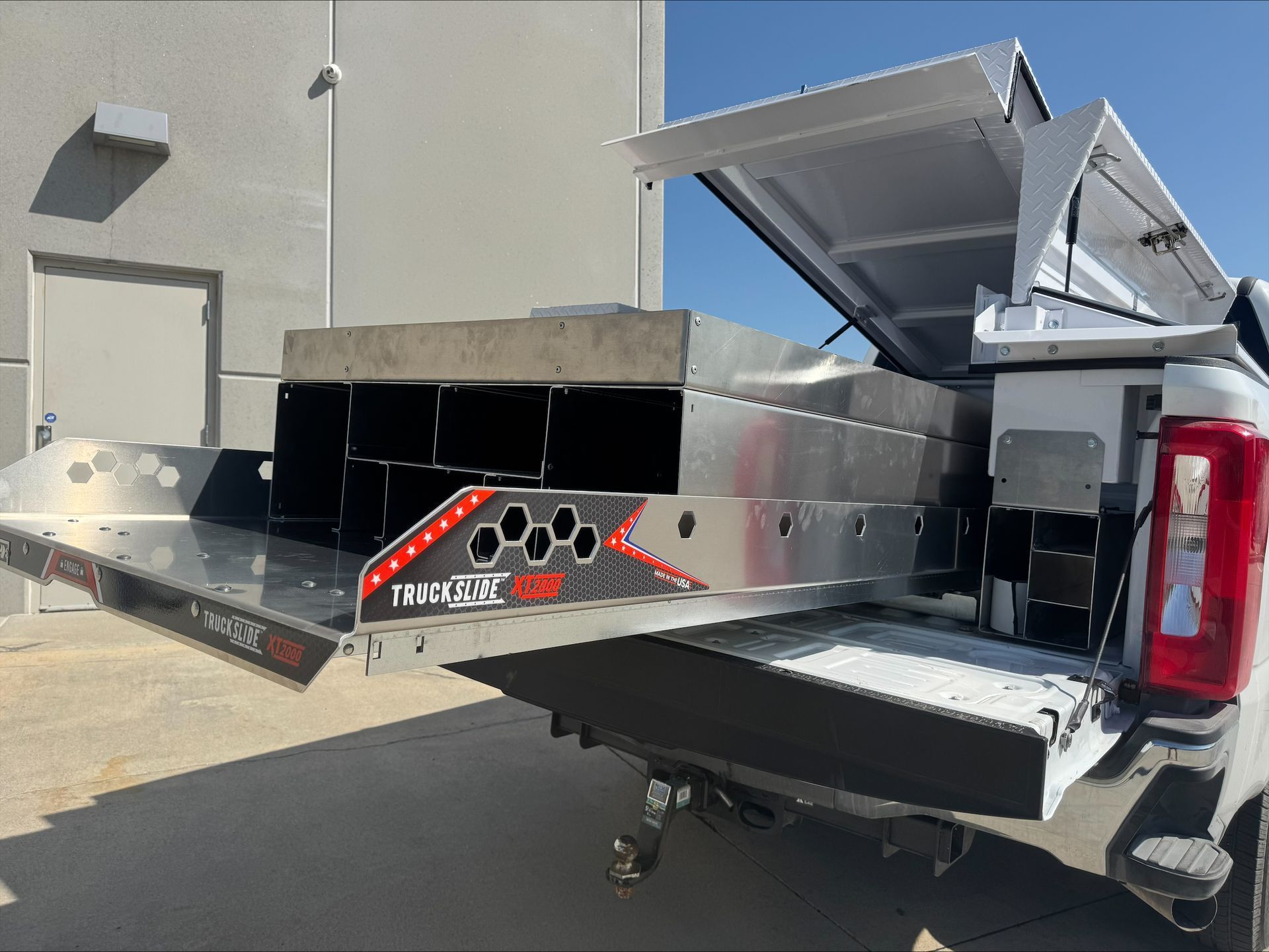 Pickup truck with an open rear utility box and metal cargo tray extended out at a building exterior.