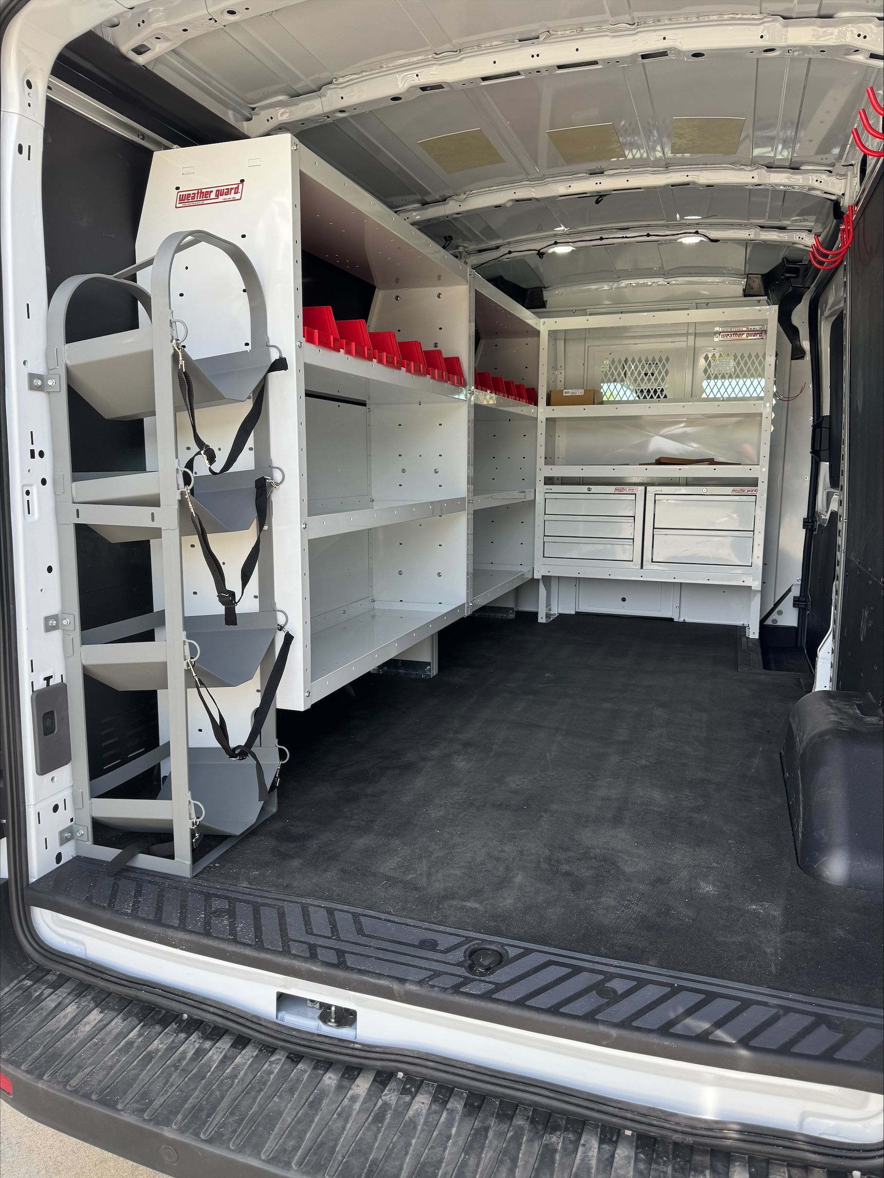 Interior of a white utility van with built-in shelves, drawers, and a ladder on the left wall.