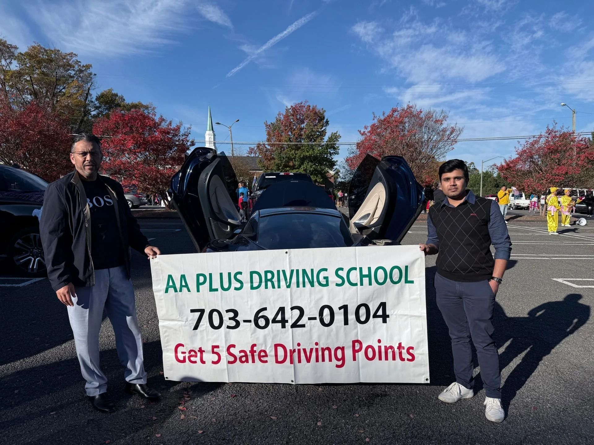 Two men holding a banner for AA Plus Driving School in front of a car with doors open.