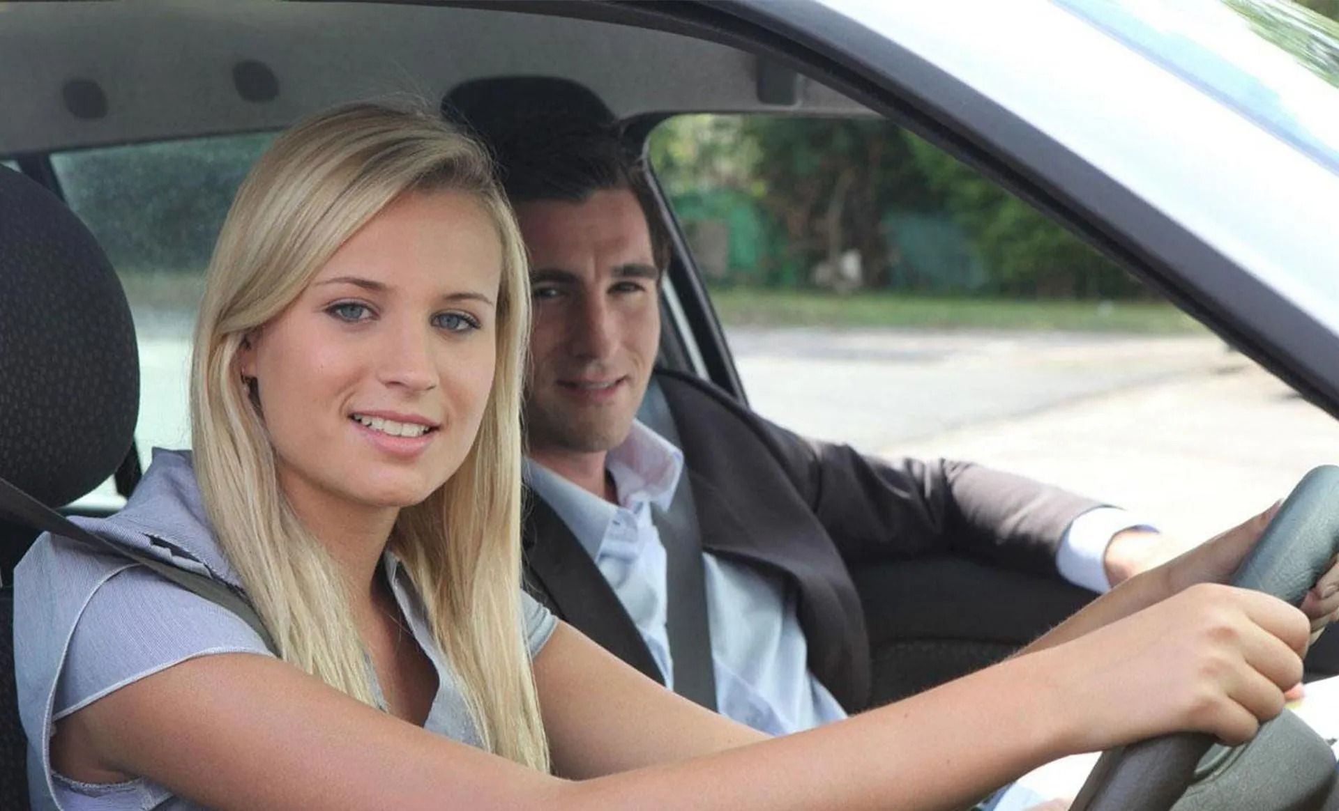 Woman driving, man in passenger seat, both smiling, inside a car.
