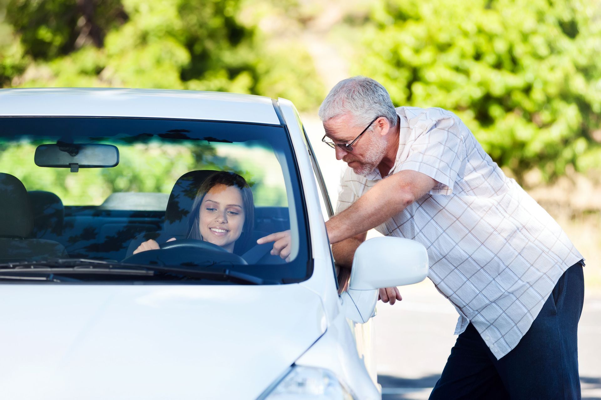 Woman in driver's seat, being instructed by older man leaning into the car.
