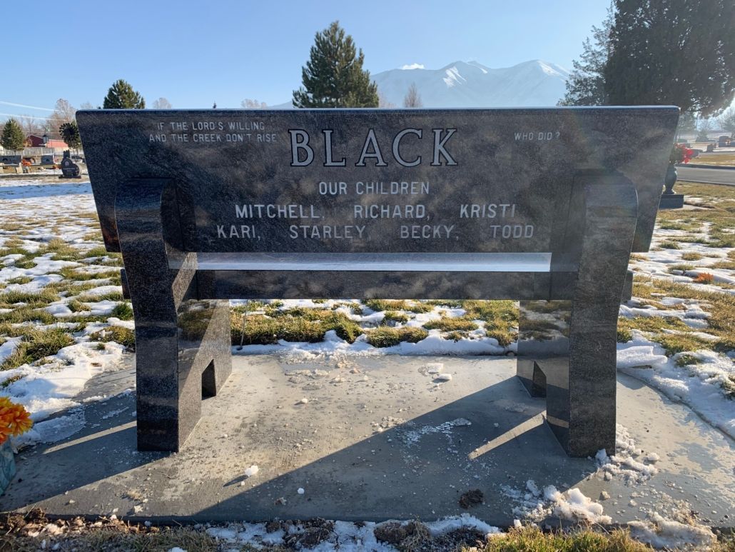 Black granite bench headstone in a snowy cemetery, with names etched on the backrest.