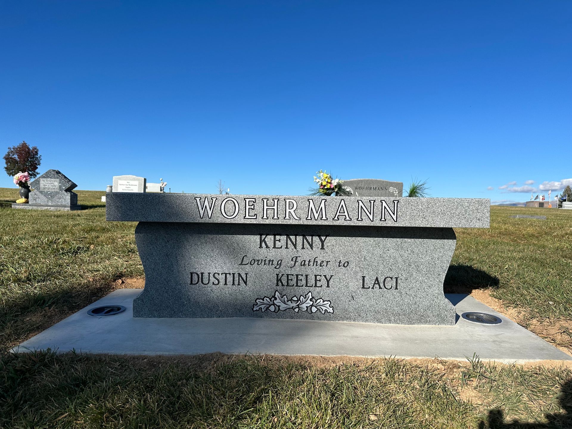 Gray granite bench-style headstone in a cemetery; inscription reads Kenny, with names of children.