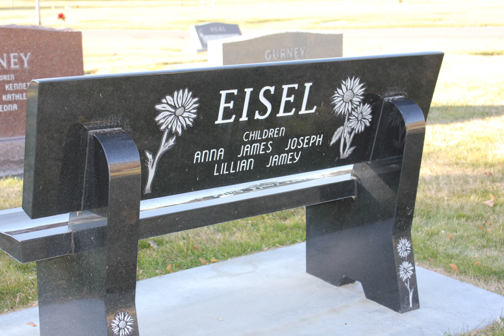 Black granite bench with EISEL and names engraved, decorated with flower motifs, in a cemetery.