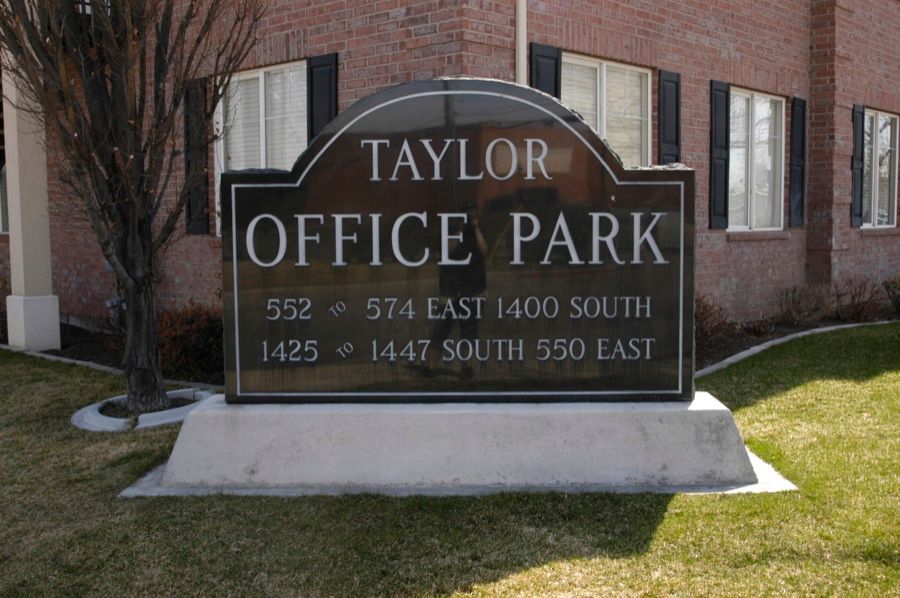 Sign for Taylor Office Park, brown with white lettering, addresses listed, on green grass.