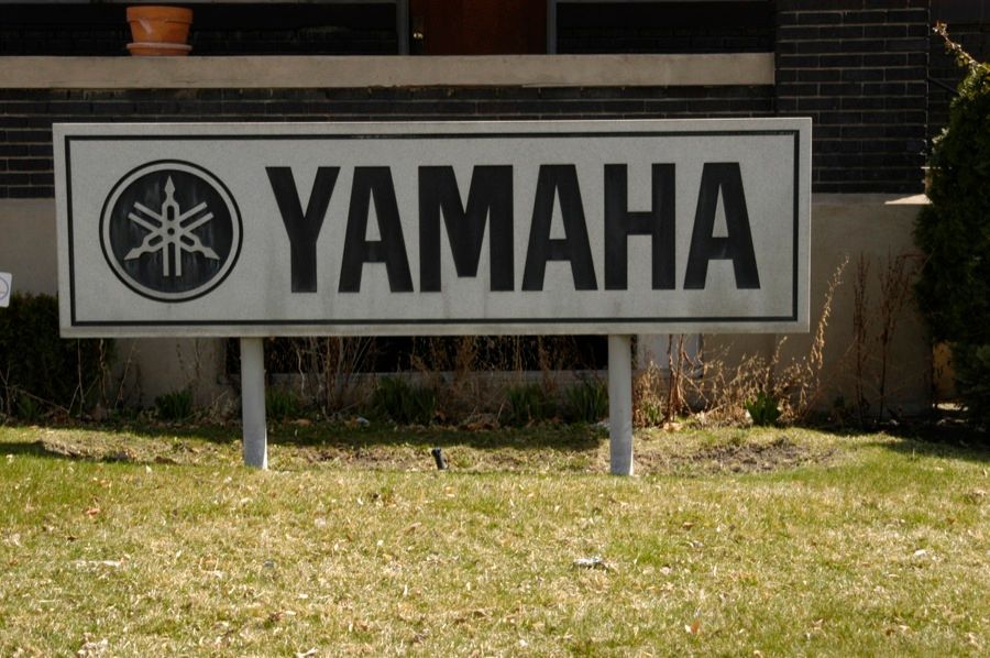 Yamaha sign in front of a building, logo with three tuning forks inside a circle, on green grass.